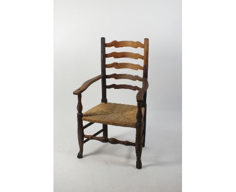 A rush seat ladder back open arm chair, 19th century, on club front legs joined by a mirrored baluster stretcher, with repair