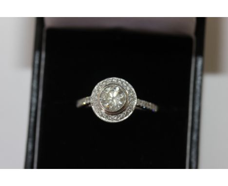 A diamond ring, the round brilliant cut stone set within a border of smaller stones, pave set gallery and shoulders