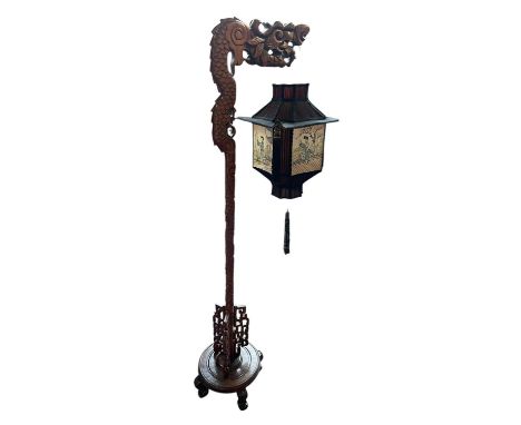 An early 20th century Chinese carved standard lamp, with silk shade decorated with four panels depicting figures in landscape
