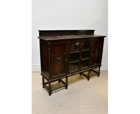 A 1920s oak bookcase, with raised back above two glazed and two panelled doors, on barley twist stretchers terminating on bob