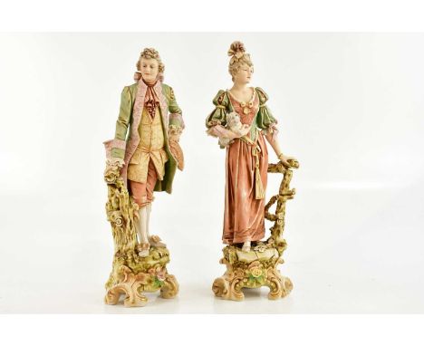 ROYAL DUX; a pair of ceramic figures representing a gentleman and lady wearing Victorian clothing, the lady clutching a puppy