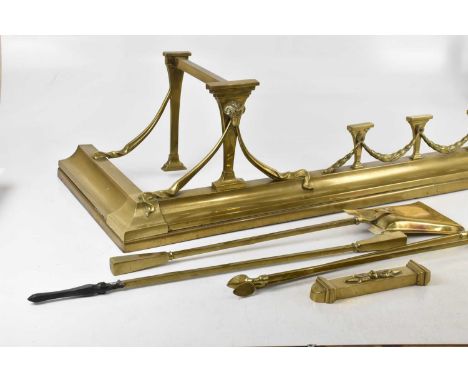 A 19th century Regency style brass fender, decorated with ram's heads and swags, width 140cm, and a brass three piece compani