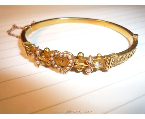 A pretty Bangle with safety chain marked SU15ct and featuring a hearth motif flanked by foliage and set with 20 seed pearls, 