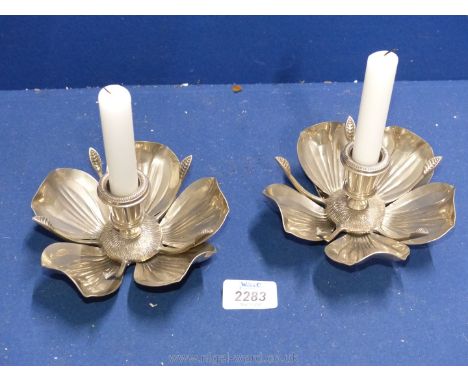 A pair of white metal candlestick holders in the form of flowers, with removable petals that form an ashtray.