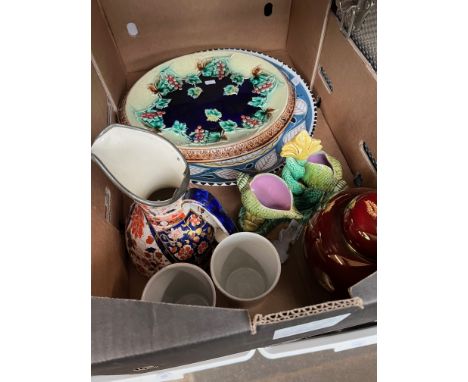 A box of various ceramic items including a Majolica bread plate, a pair of 1922 Preston Guilt beakers, a Majolica dolphin dou