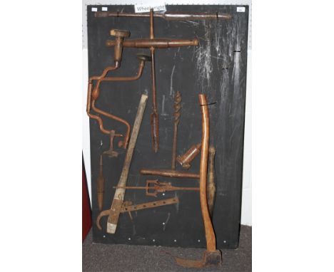 A collection of assorted vintage wheelwright tools on a display board. Including adze, auger, etc.