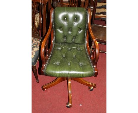 A reproduction mahognay and green leather buttoned and further studded scroll swivel desk chair, raised on roller castors, wi