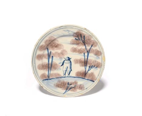 An unusual delftware plate, c.1730-40, painted with a short figure wearing a hat, flanked by tall trees sponged in manganese,