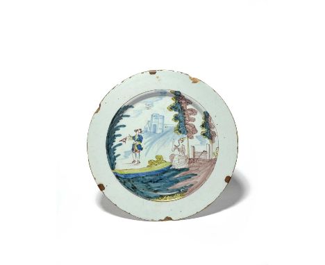 A London delftware large plate or charger, c.1765, painted in blue, green, yellow and manganese with a lady beckoning to a ge