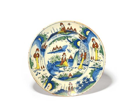 A large delftware charger, c.1720-30, probably London, painted in polychrome enamels with Chinese figures in a garden setting