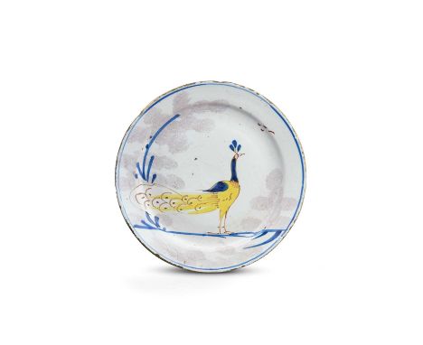 A Bristol delftware 'Farmyard' plate, c.1720-30, painted in yellow, blue and red with a proud peacock between trees sponged i