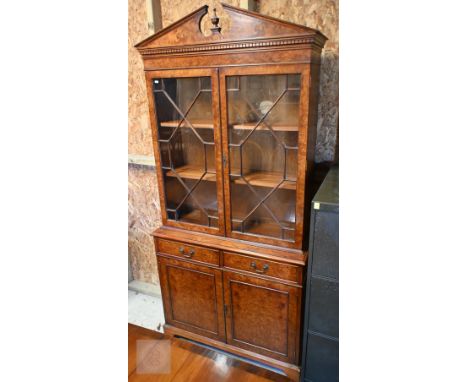 A reproduction Georgian style burr walnut chiffonier bookcase, the broken arch pediment over a pair of astragal glazed cabine