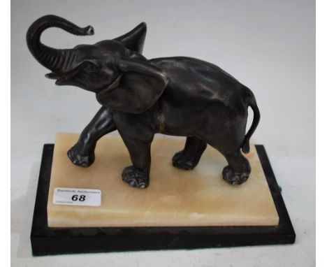 An Art Deco animalier bronzed metal Elephant, modelled walking trunk erect in challenge, sloping two tone cream and black ony