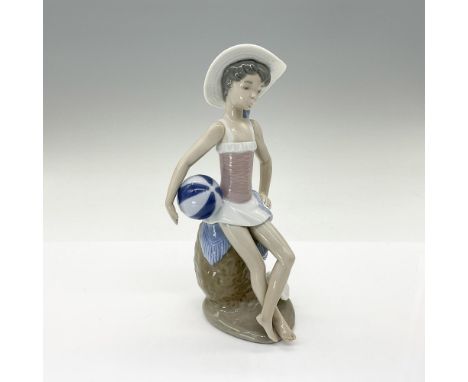 This glossy-finished figurine depicts a young girl standing with a beach ball, embodying the joy and carefree spirit of summe