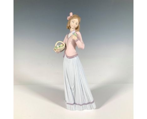 A young woman in a soft pink sweater and long periwinkle skirt holds a basket of flowers in her hands, gently placing one ove