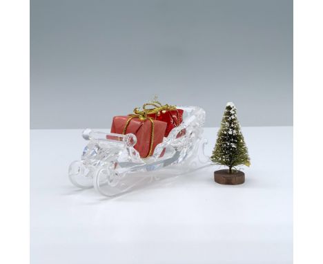 A clear and fogged crystal figure that depicts a sled and includes four Christmas prop items, a pine tree and three gift wrap