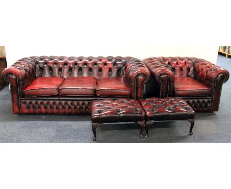 A button backed, ox blood leather, three seater Chesterfield settee with matching armchair and two foot stools.