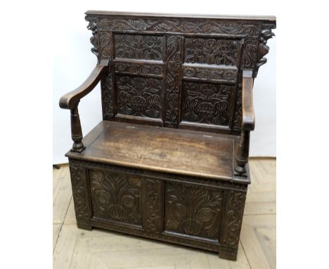 C20th oak settle, raised scroll work back with four earlier carved and initialled panels, moulded down scroll arms and hinged