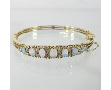 A 9 carat gold opal and diamond set bangle, of hinged design, set with single row of seven graduated oval opals, with safety 