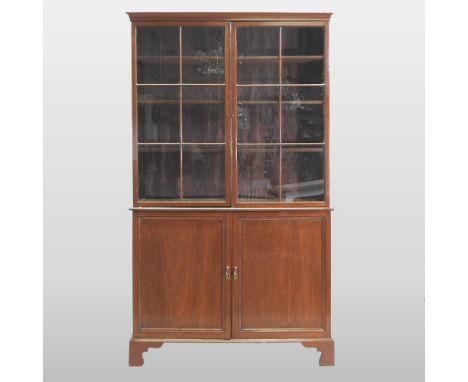 An early 20th century mahogany cabinet bookcase, the upper section fitted with shelves and enclosed by a pair of astragal gla