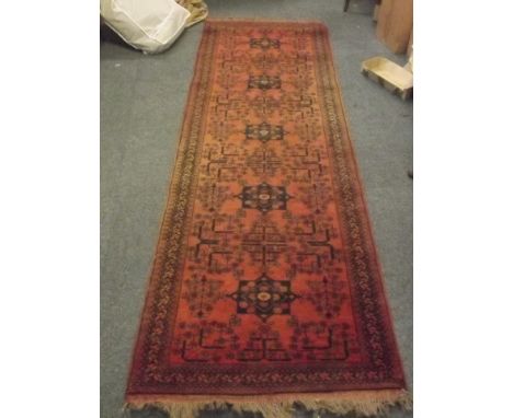 A long red ground carpet runner with tasselled ends, 110'' x 34''