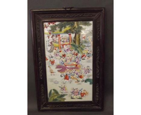 A C20th Chinese ceramic plaque decorated with boys playing, in a carved wooden frame, 28'' x 16''
