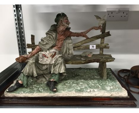 A large Capo di Monte style figure modelled as a Tramp seated on a bench.