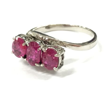 A white metal (possibly platinum) three stone ruby ring.