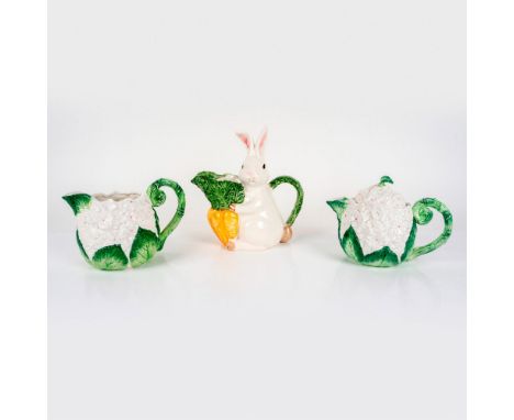A covered teapot and pitcher molded with white flowers and large green leaves; vine coil handle. A pitcher shaped as a white 