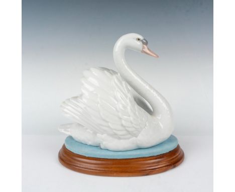 Glossy finish; enchanting white swan swims gracefully in the serene waters. Sits on a wooden base lined with blue fabric repr