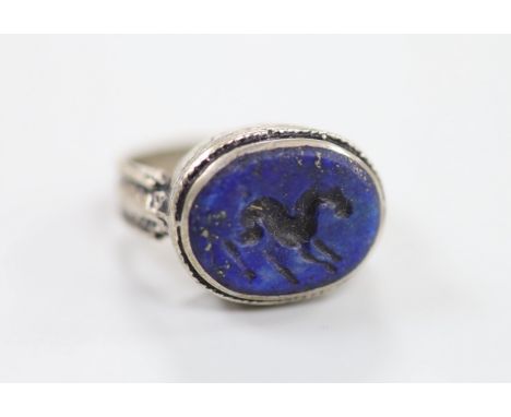 An engraved white metal and intaglio lapis lazuli set oval ring, the matrix carved with a horse?, size R/S, gross weight 7.4 