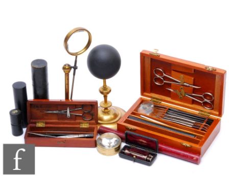 A 20th Century mahogany cased set of scalpels with scissors, a similar smaller set, a magnifying glass on stand, a black sphe