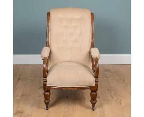 A Victorian oak-framed armchair With button-back cream upholstery and scrolling arms raised on reeded feet with brass caps an
