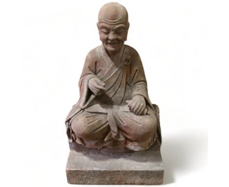 A large and impressive Chinese seated figure carved from a single block of stone, the figure holding a prayer scroll and seat