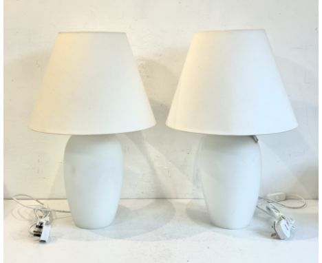 A pair of opaque white glass 'light-up' table lamps - the ovoid glass lamps with bulbs above and below the fitting, lighting 