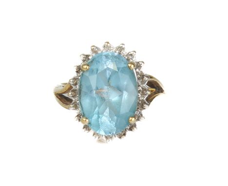 An 18ct yellow gold, topaz and diamond cluster ring - import hallmarks London 1992, the 14 x 10mm oval cut blue topaz within 