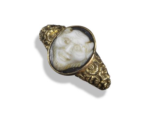A carved hardstone cameo ring, the cameo depicting the head of a satire, in gold mount with foliate and shell engraved shank,
