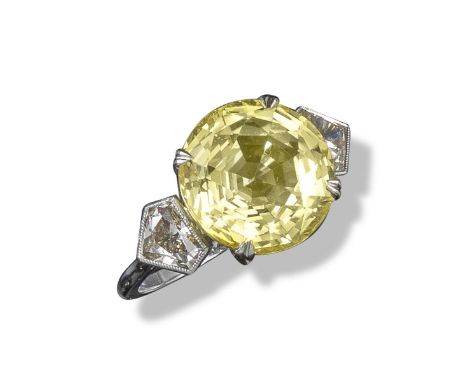 A yellow sapphire and diamond three-stone ring, the circular-cut yellow sapphire weighs 8.97cts and is set in platinum with a