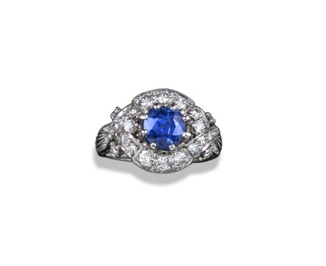 A sapphire and diamond cluster ring, the cushion-shaped sapphire weighs approximately 2.70cts and is set within a surround of