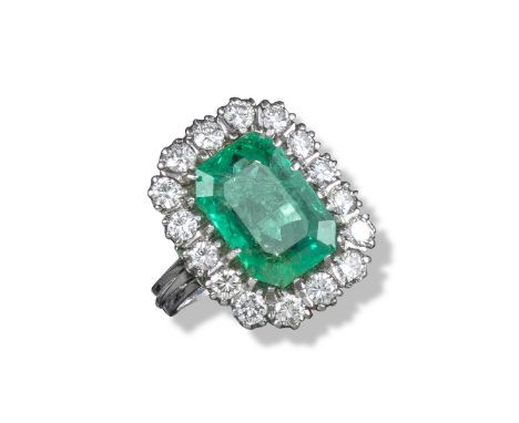 An emerald and diamond cluster ring, the emerald-cut emerald weighs approximately 6.20cts and set within a surround of sixtee