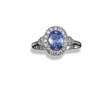 A sapphire and diamond cluster ring, the oval-shaped sapphire set within a surround of round brilliant-cut diamonds in white 