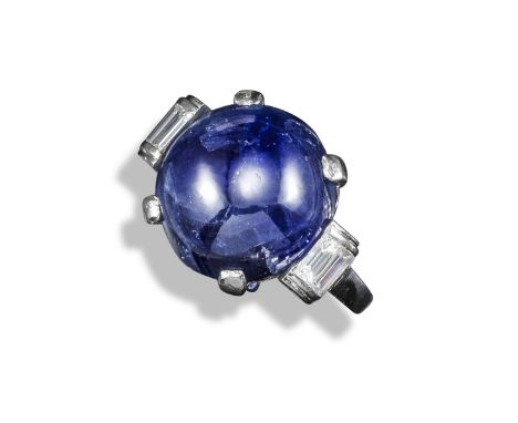 A sapphire and diamond ring, the circular sapphire cabochon flanked within baguette-shaped diamond scroll shoulders in platin