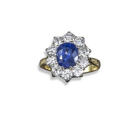 A sapphire and diamond cluster ring, the oval-shaped sapphire set within a surround of ten round brilliant-cut diamonds in ye