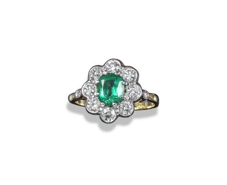 An emerald and diamond cluster ring, the oval-shaped emerald weighs approximately 1.10cts and is set within a surround of eig