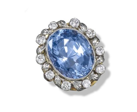 A large sapphire and diamond cluster ring, the oval sapphire is set within a border of stylised leaves and circular-cut diamo