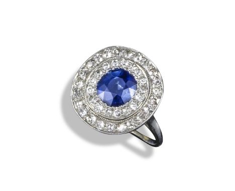 A sapphire and diamond cluster ring, the oval-shaped sapphire is millegrain-set within two surrounds of circular-cut diamonds