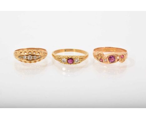 Three antique 18ct gold diamond and gem set rings in carved scroll settings to include a diamond five stone ring, ruby and di