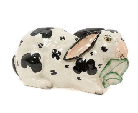 Staffordshire pottery model of a rabbit, circa 1850, painted in black and white and shown nibbling on leaves, 24cm longThere 