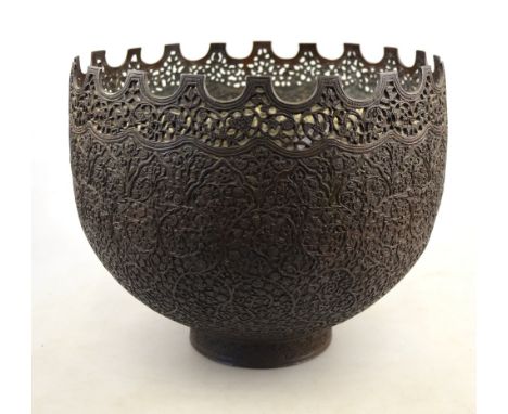 An antique Persian bowl cast overall with a foliate filigree pattern and having a crenulated pierced rim raised on a circular
