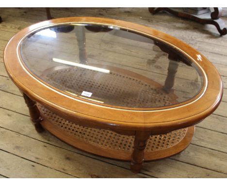 A modern oval glass top coffee table with rattan shelf below